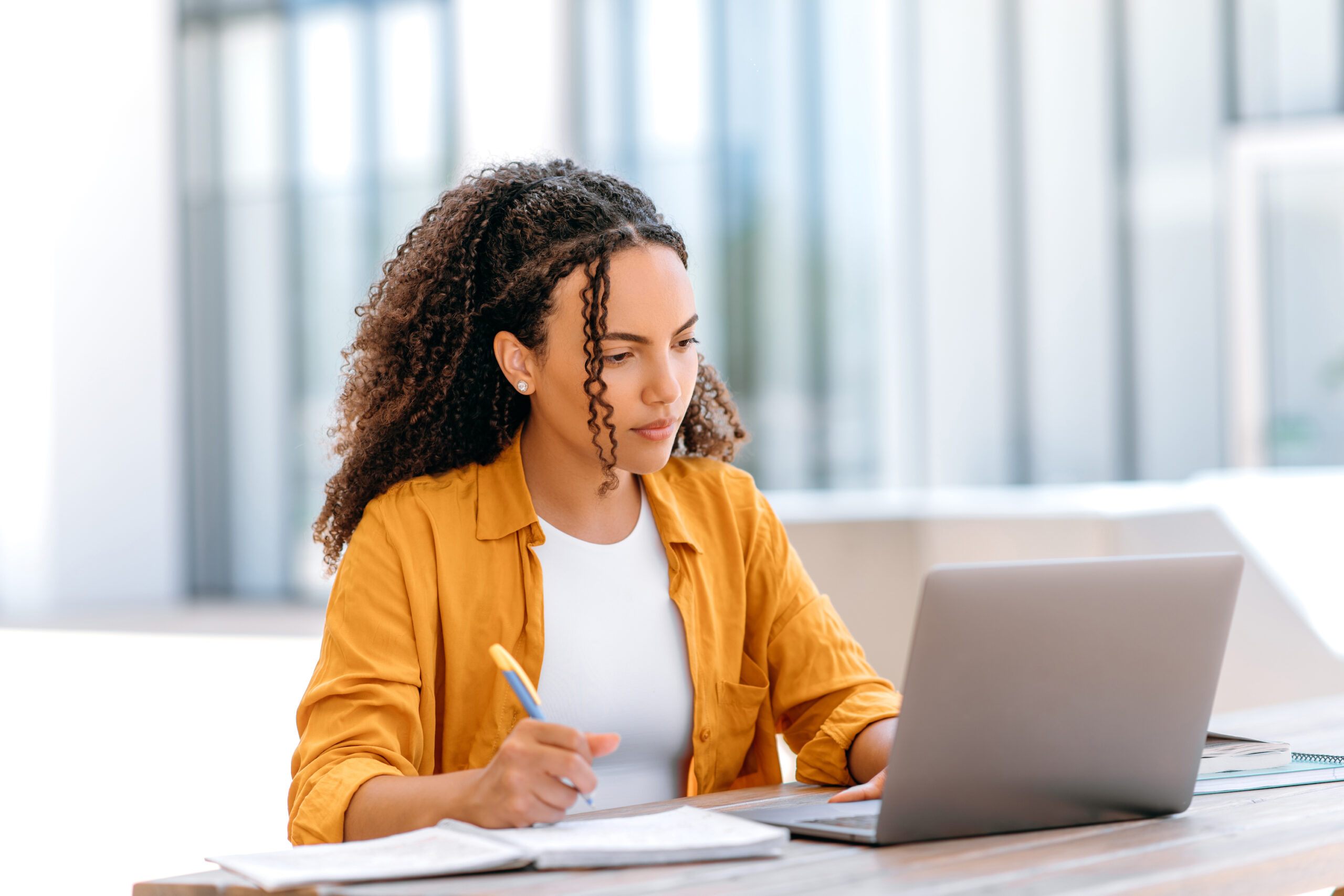 Successful smart student, uses laptop to work or study online while sitting outdoors, takes notes in notebook